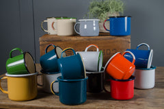 Colorful vintage enamel mugs on a wooden table with a gray wall background