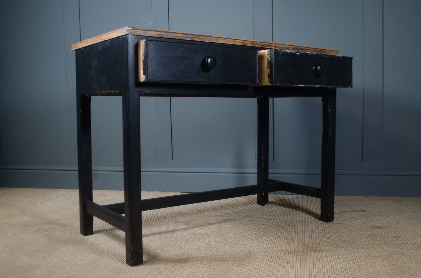 Black desk with wooden top against a gray wall