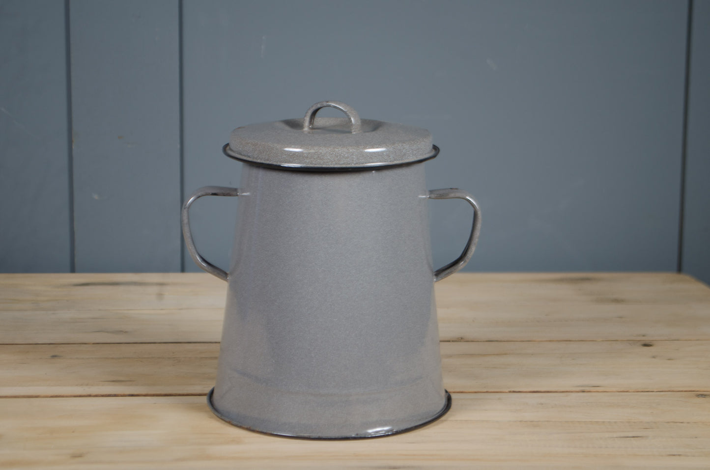 Grey enamel storage tin with lid on a wooden surface against a blue wall