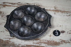Black metal mold with six round cavities on a rustic wooden surface for eggs
