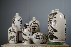 Set of white ceramic bottles with black text on a wooden surface against a gray wall. japanese sake bottle