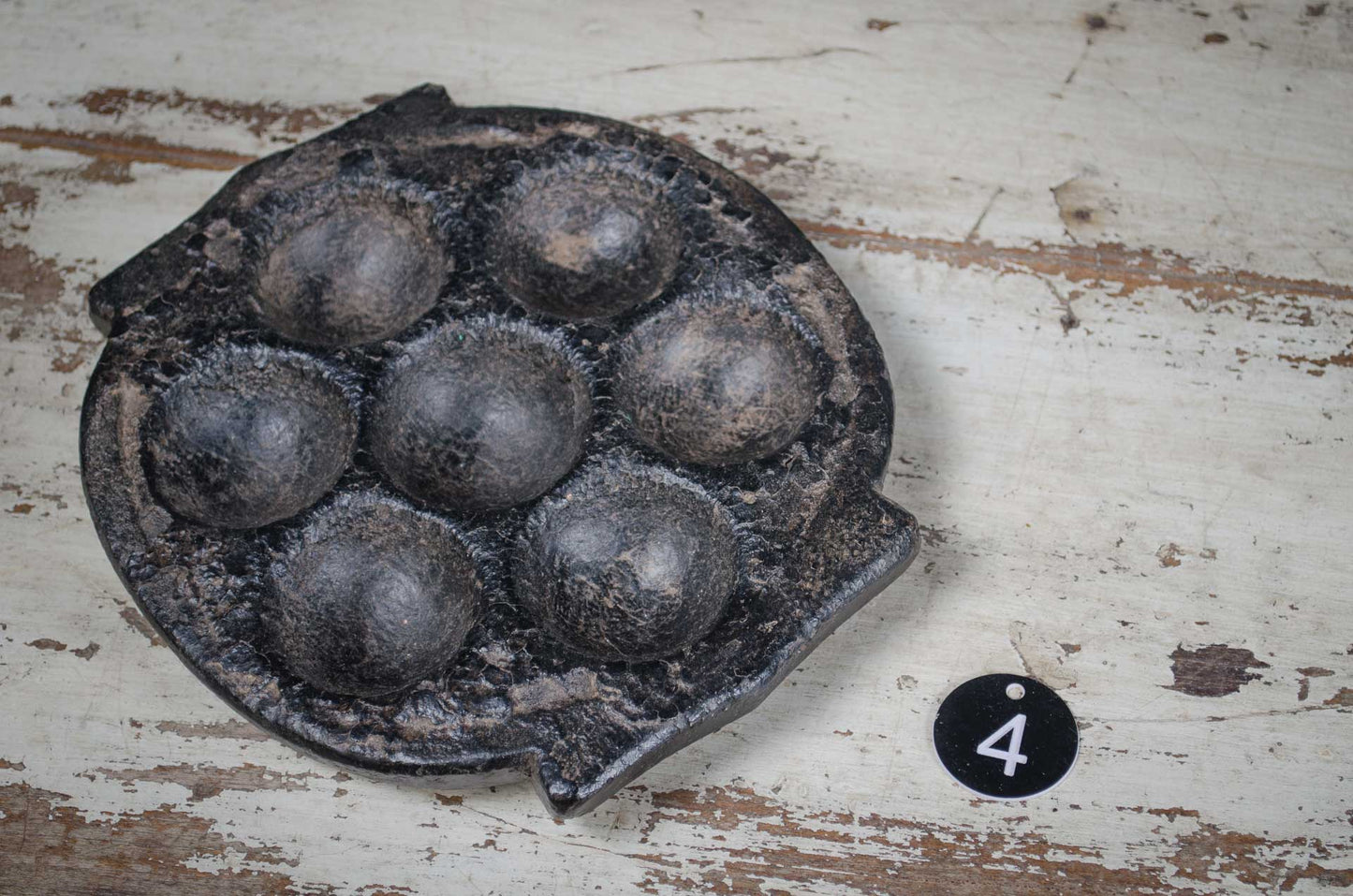 Vintage metal waffle iron on a rustic wooden surface with a number '4' tag.