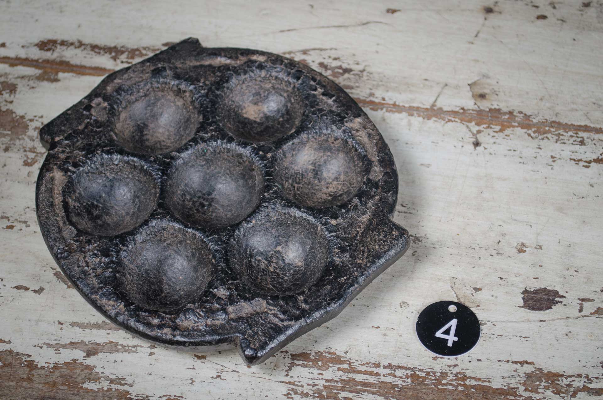 
Vintage metal waffle iron on a rustic wooden surface with a number '4' tag.
