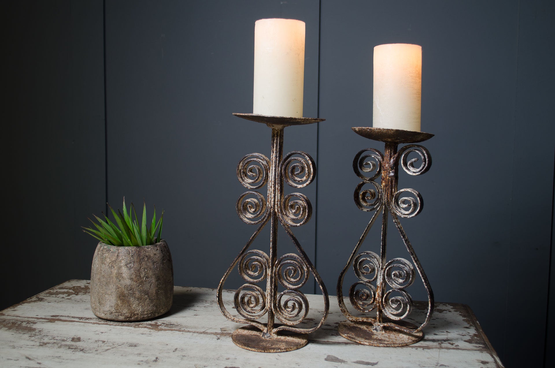 Two ornate metal candle holders with candles on a rustic surface against a dark background