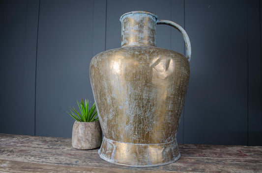 Large antique brass water jug with weathered verdigris patina, polished finish, and handle, displayed on rustic wooden surface.
