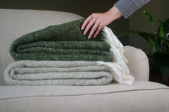 Person arranging folded lambs wool tail blankets on a couch with a plant in the background