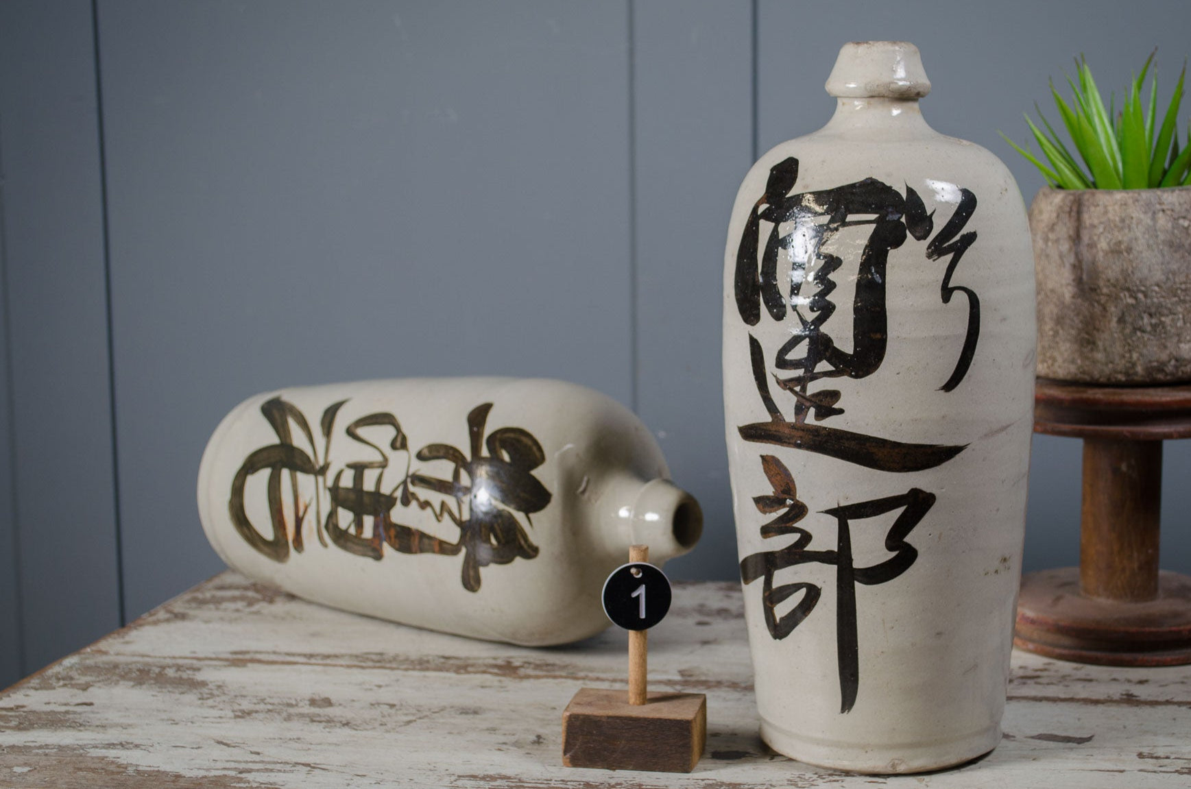 Sake Two ceramic bottles with black text on a wooden surface against a gray wall.