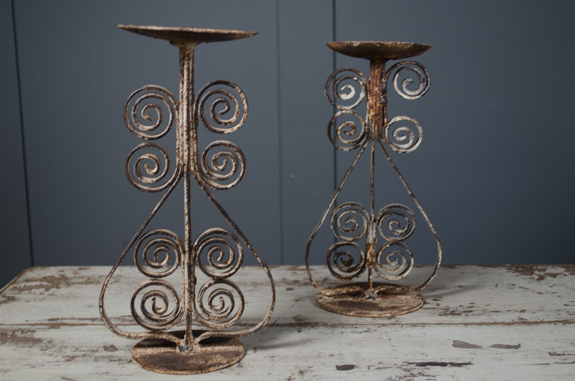 Two wrought iron candle holders with spiral designs on a wooden surface against a gray wall.