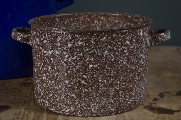 Brown speckled enamel pot on a wooden surface with a dark background