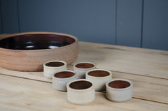 Decorative stoneware serving bowl with six matching ramekins in earthy black and rust tones.