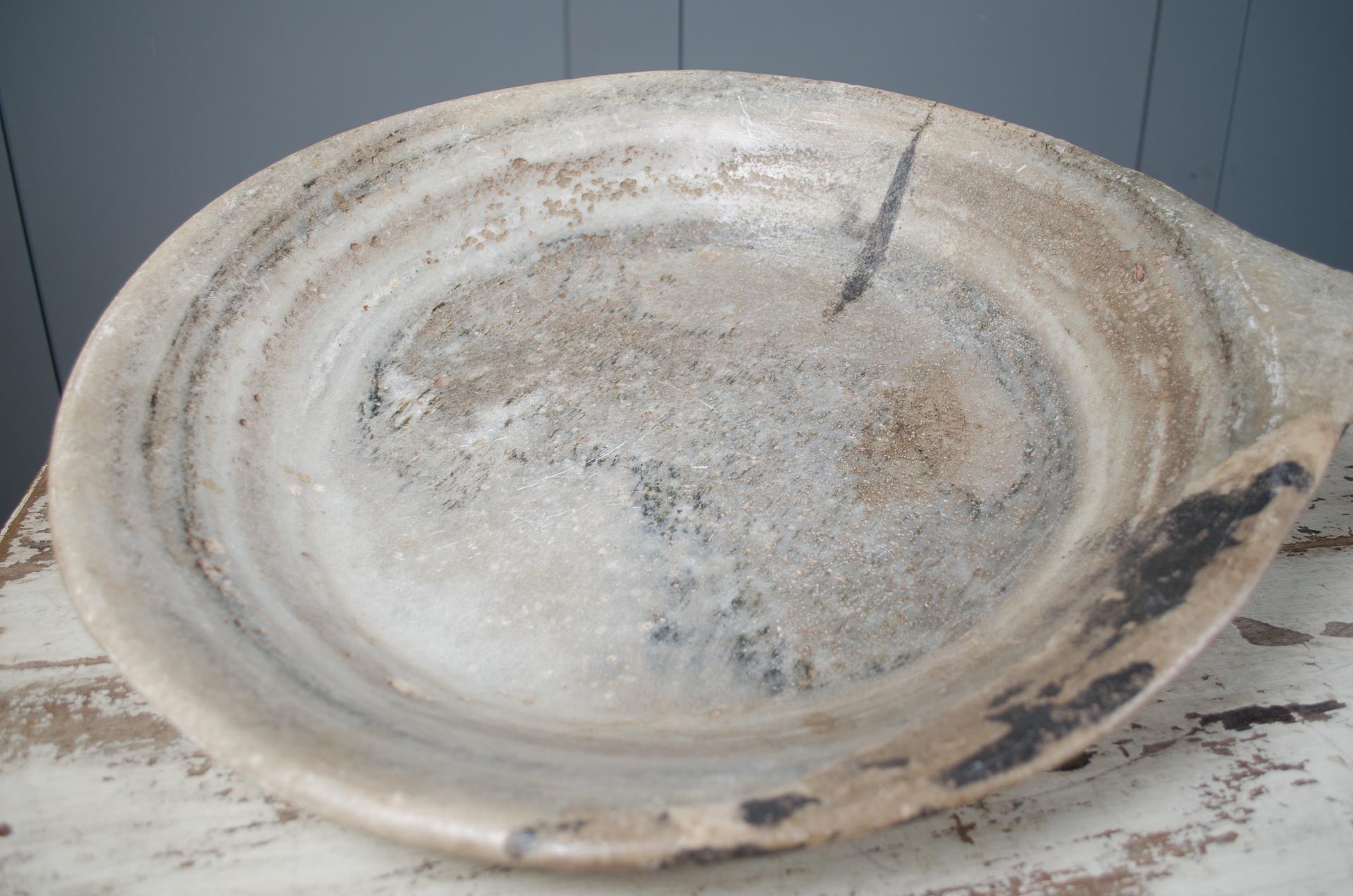 Large ceramic dish with a rustic, worn appearance on a wooden surface.