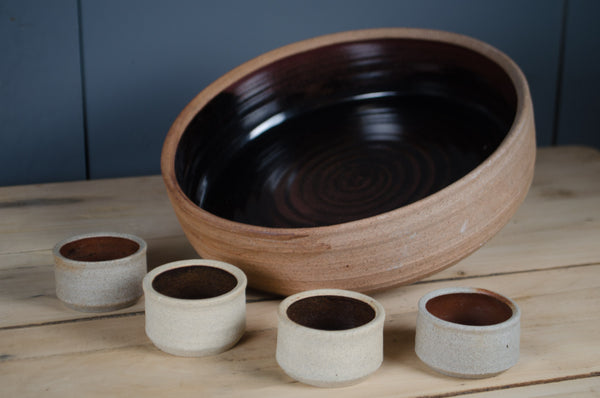 Hand-thrown French stoneware serving bowl with six matching ramekins in a black and rust reactive glaze.