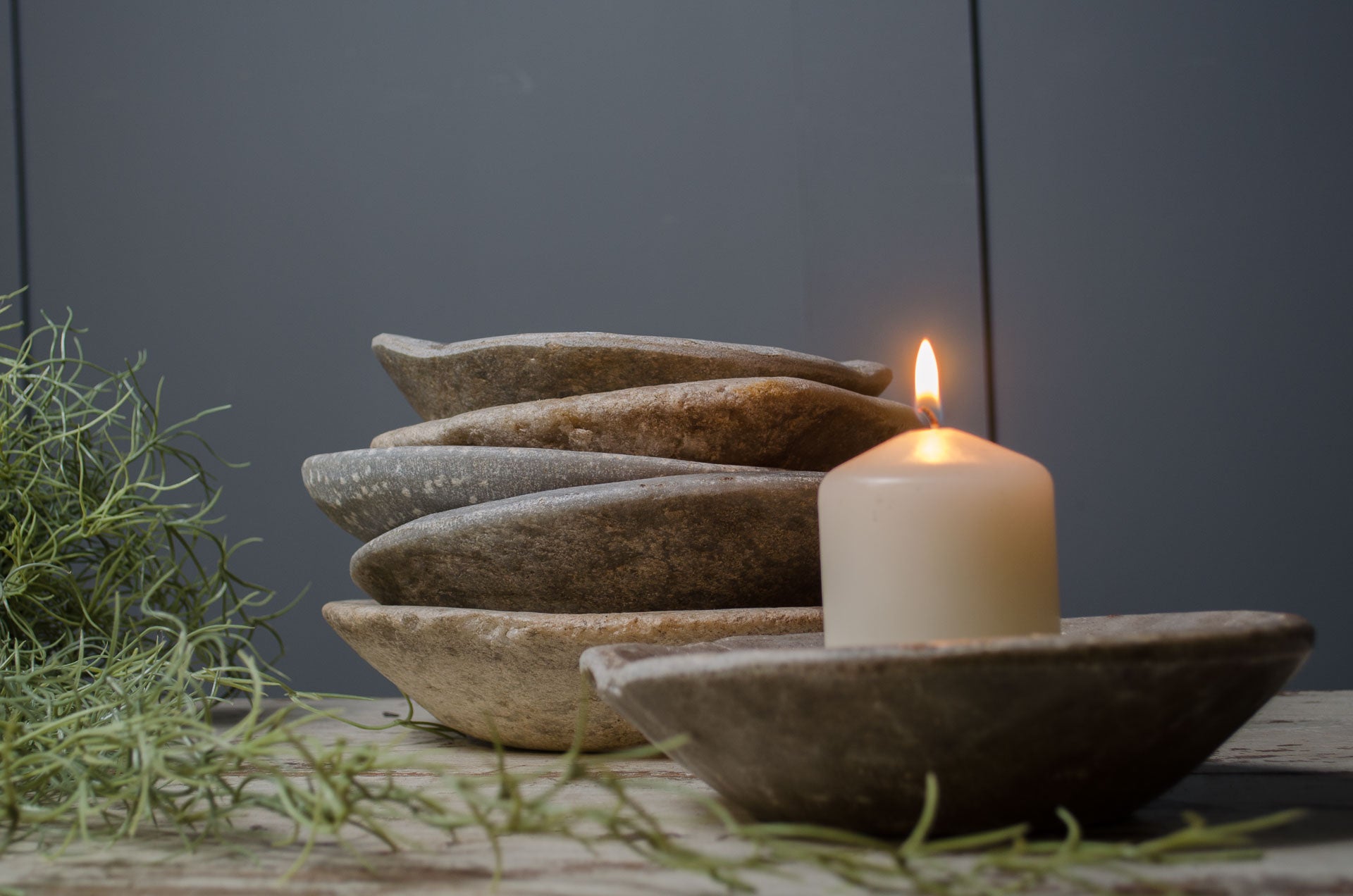 Decorative stone bowls with a lit candle on a wooden surface with grass.