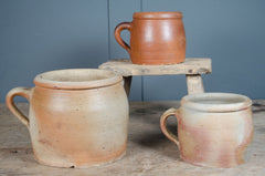 Three french stoneware rustic confit terracotta mugs on a wooden surface with a blue wall background