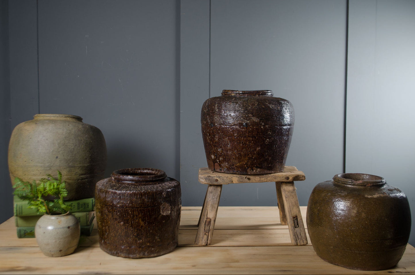 Collection of brown ceramic jars on a wooden surface with a gray wall background