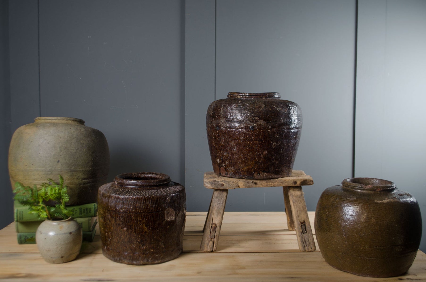 
Collection of brown ceramic jars on a wooden surface with a gray wall background