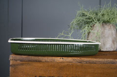 Green rectangular container on a wooden surface with a plant in the background