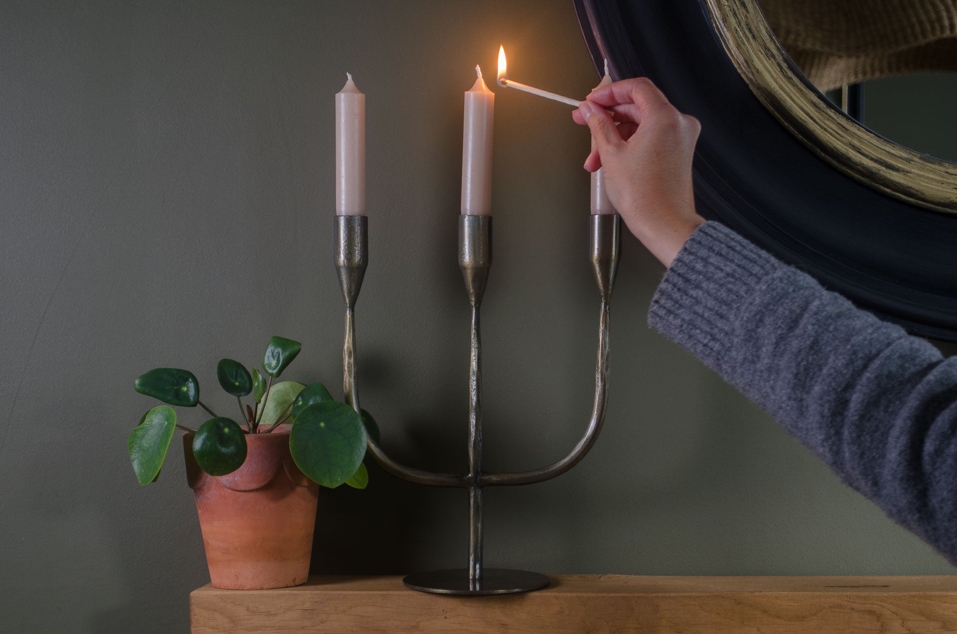 Person lighting a candle in a decorative antique brass metal candelabra on mantel table with green walls