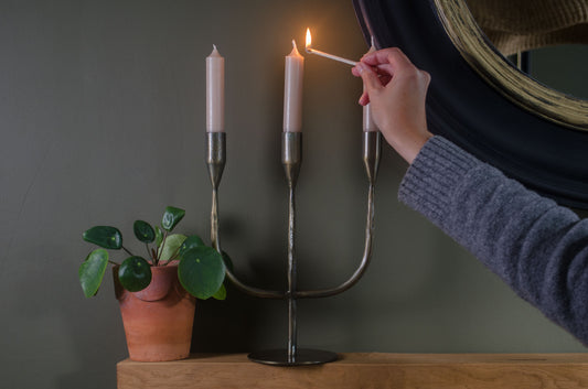 Person lighting a candle in a decorative antique brass metal candelabra on mantel table with green walls