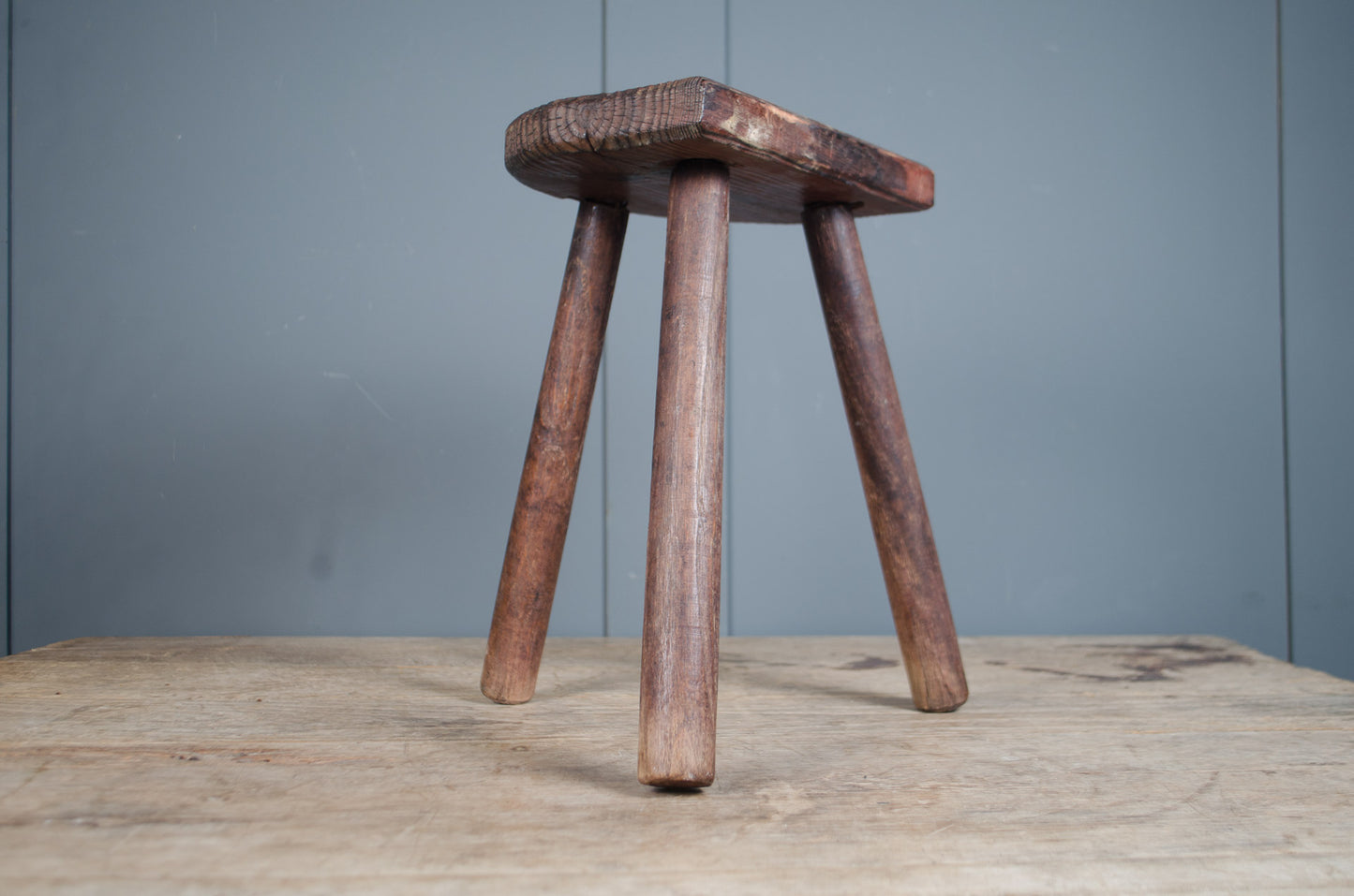 Rustic French wooden milking stool with three legs and a weathered patina, sourced from France.