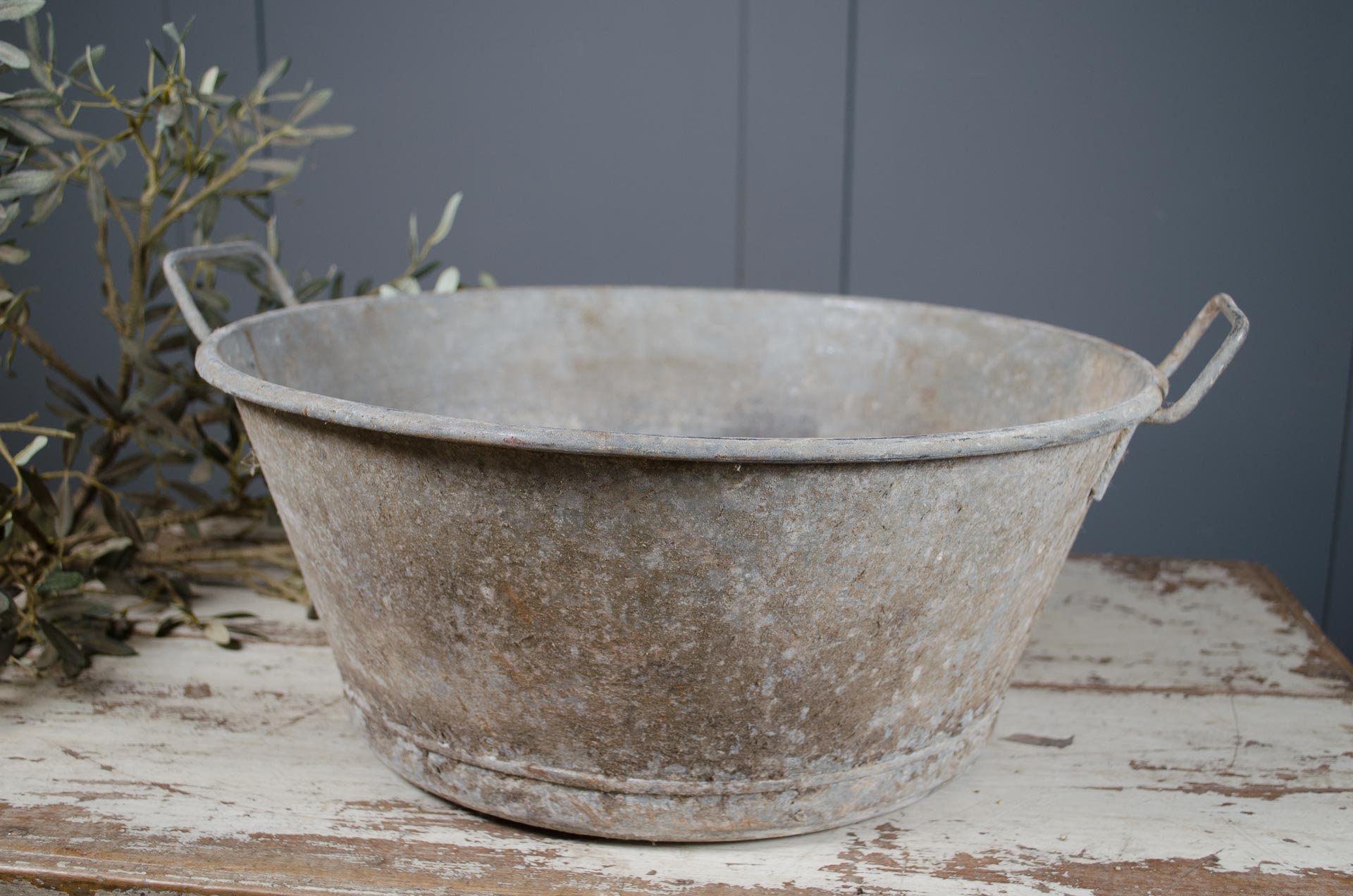 Vintage-style metal tub on a wooden surface with a gray wall background