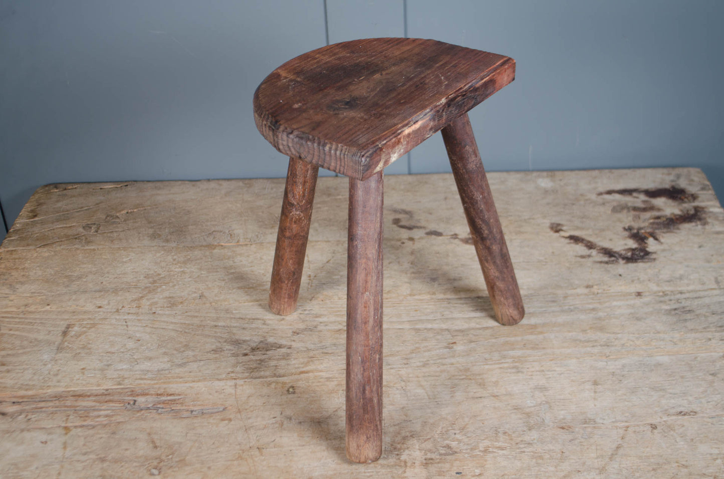 Rustic French wooden milking stool with three legs and a weathered patina, sourced from France.