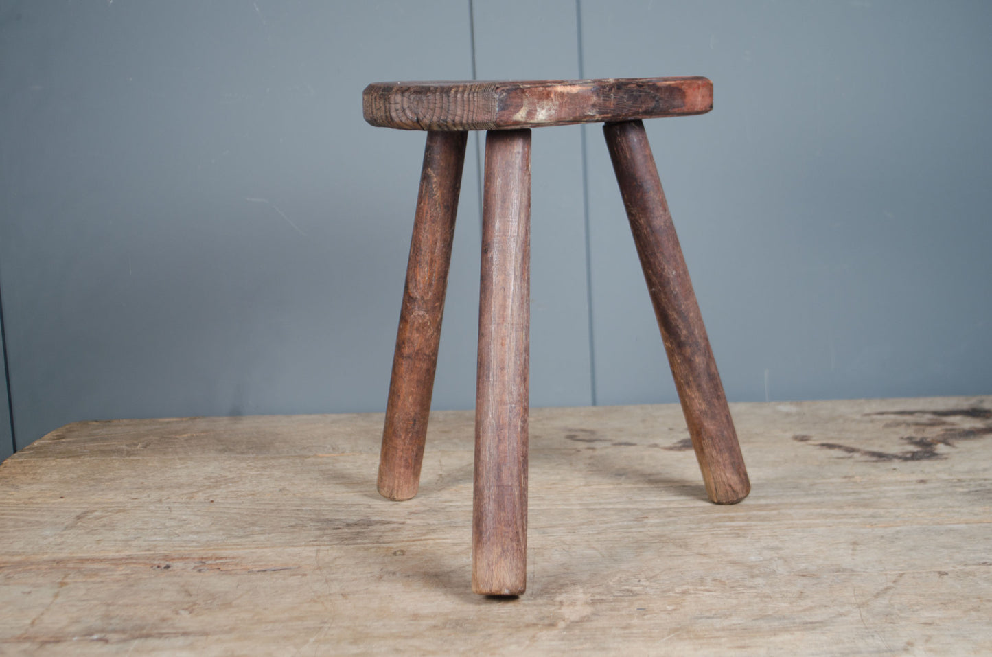 Rustic French wooden milking stool with three legs and a weathered patina, sourced from France.