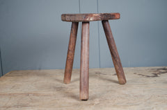 Rustic French wooden milking stool with three legs and a weathered patina, sourced from France.
