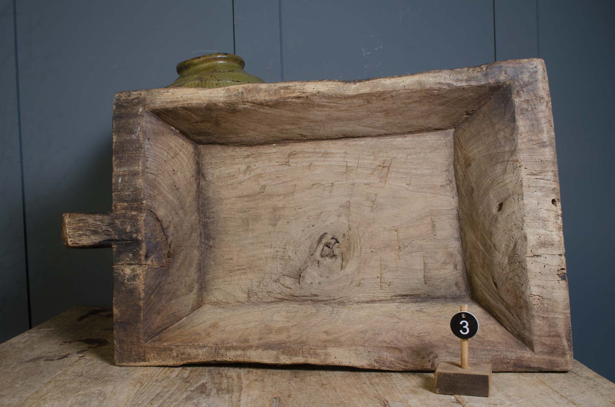 
A large, rustic rectangular wooden dough trough or planter made from weathered wood, displayed on a wooden surface against a dark gray paneled background.