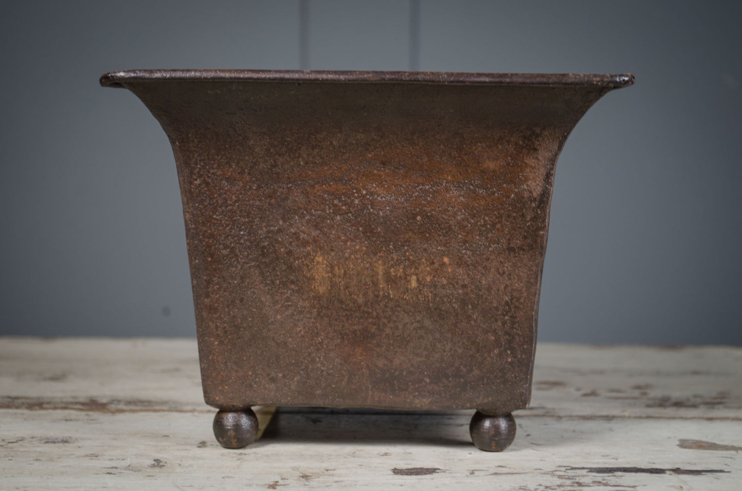 Rustic metal planter on a wooden surface with a gray background