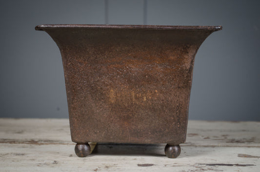 Rustic metal planter on a wooden surface with a gray background