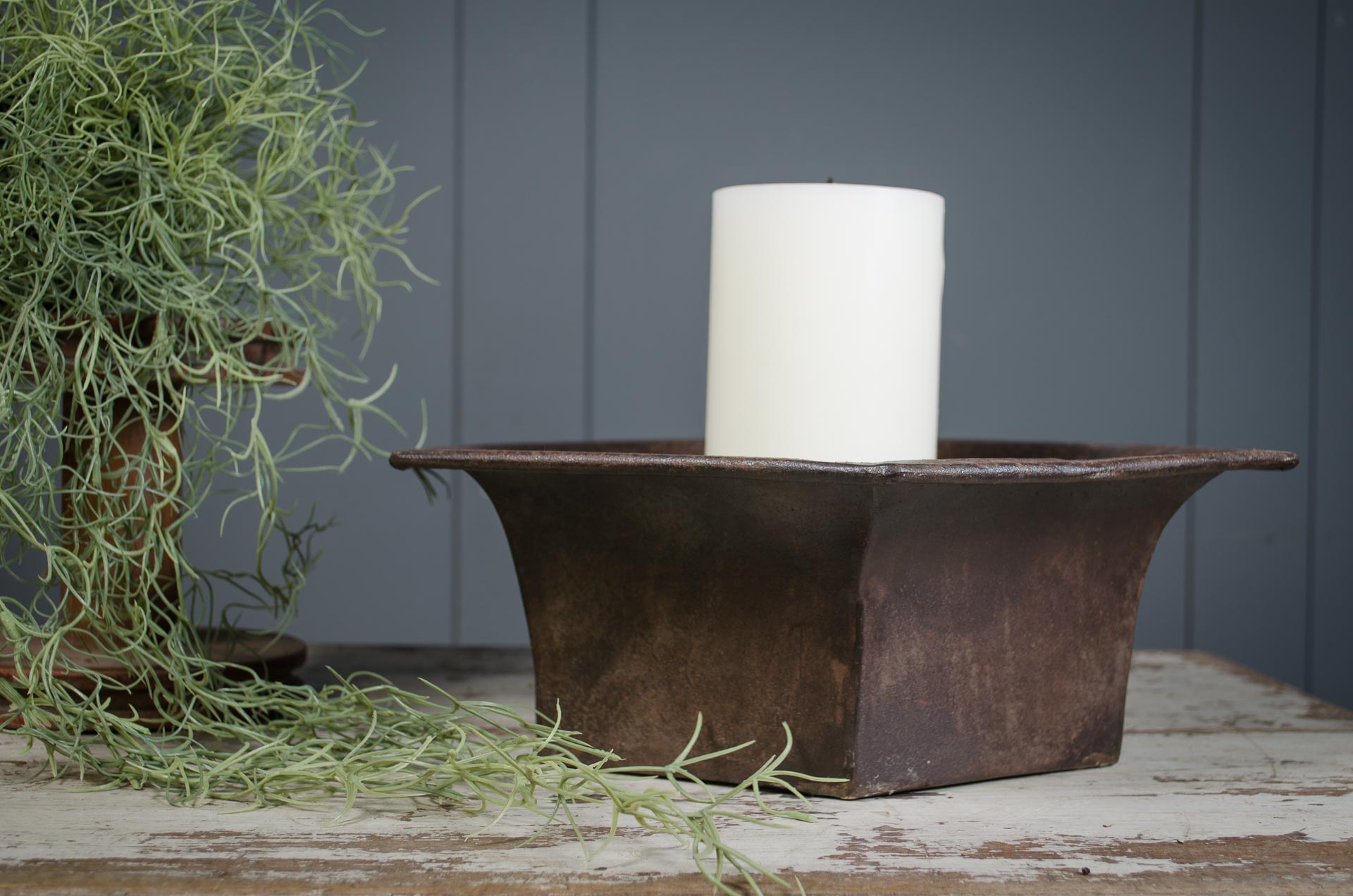 
Rustic iron metal candle holder with a white candle on a wooden surface with plants.