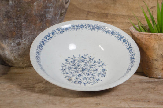A white ceramic bowl with a blue floral pattern, displayed on a rustic wooden surface next to a potted succulent and a large textured vase.