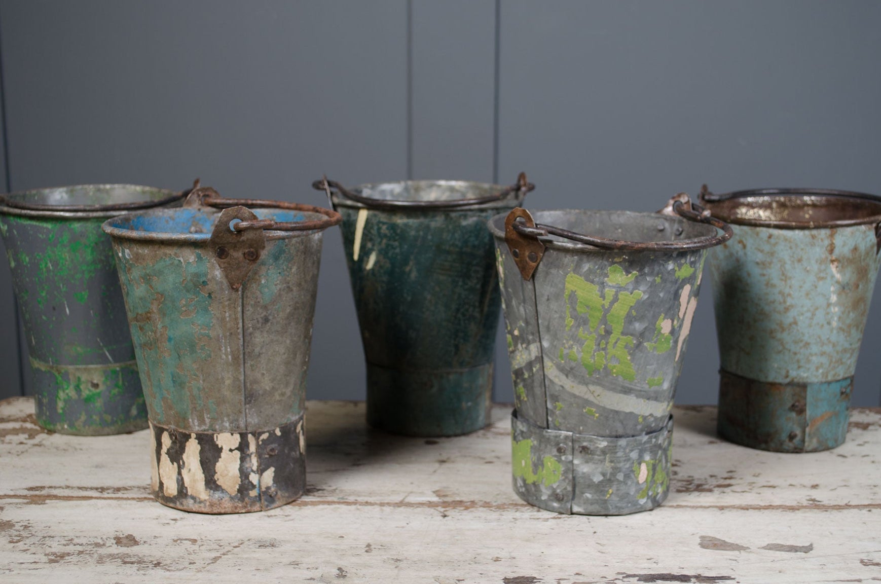 Five old, rusted metal buckets on a wooden surface with a gray background