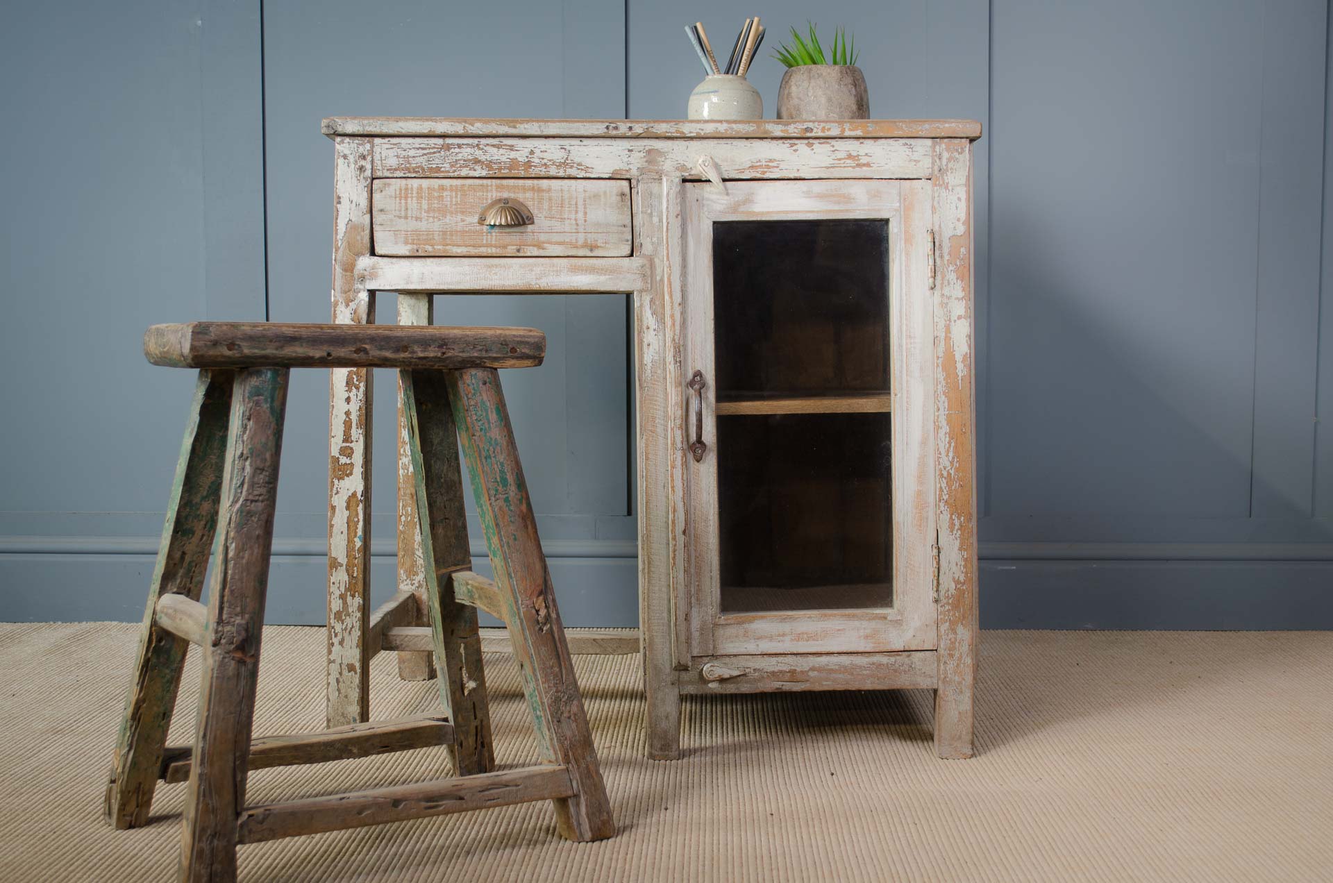 Vintage wooden cabinet with a stool against a gray wall.