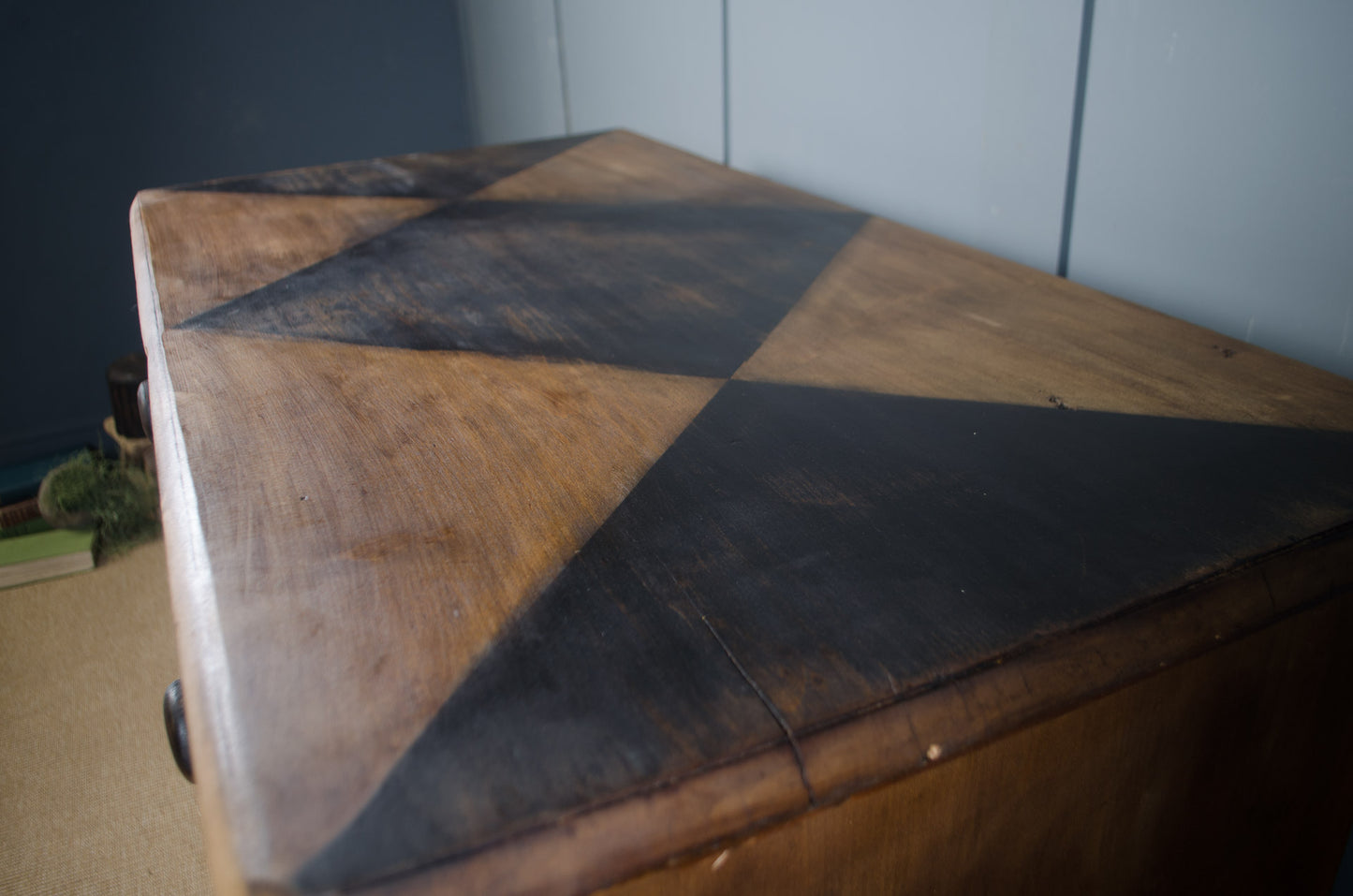 A close-up of a wooden chest or cabinet with a geometric pattern of alternating dark brown and black triangular panels on the top surface.