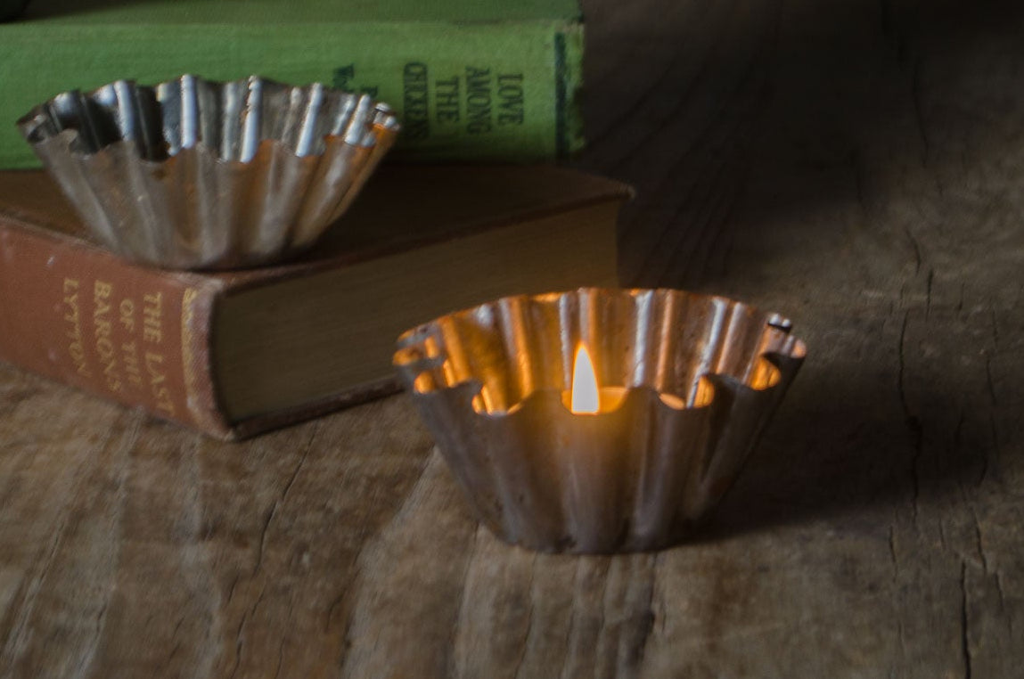 Three metallic fluted candle holders, two silver and one bronze, styled on vintage books with a rustic vase and pinecone on a wooden table.