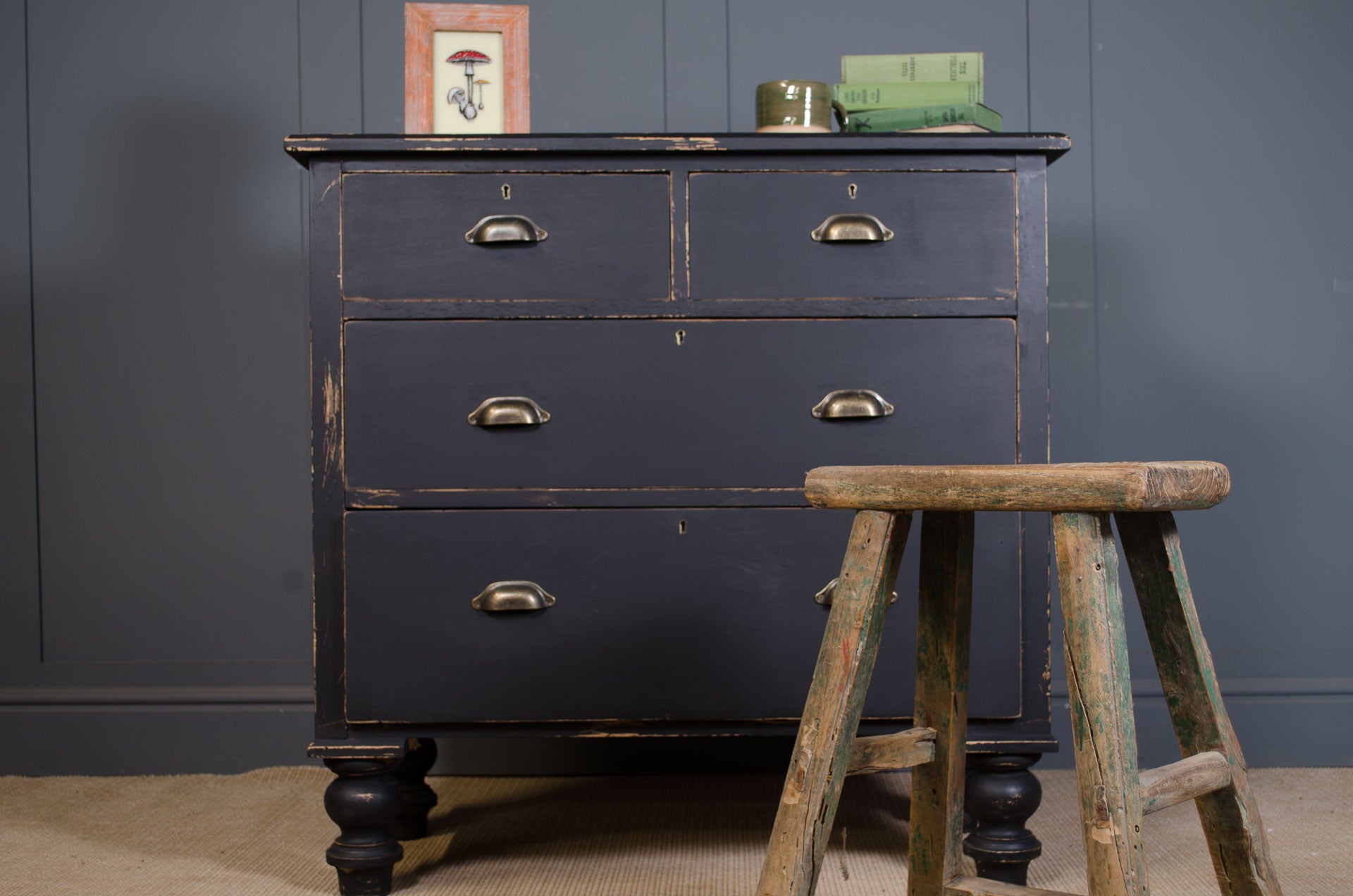 Dark grey drawers with antique gold handles  accompanied by a wooden stool.
