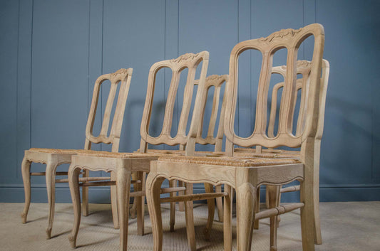 A set of six light natural wood dining chairs with carved backrests and woven seats, arranged against a blue paneled wall.