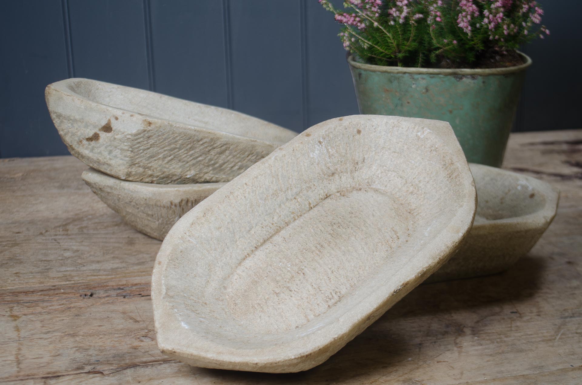 
Three stone indian spice bowls on a wooden surface with a plant in the background.