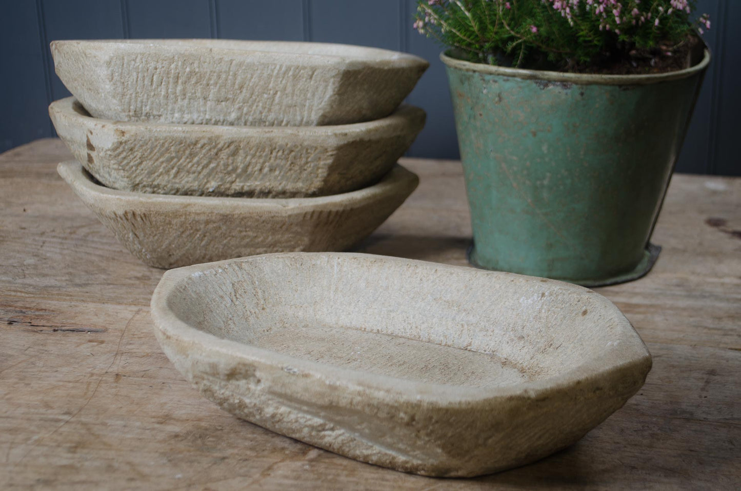 Set of stone bowls on a wooden surface with a green pot containing plants.