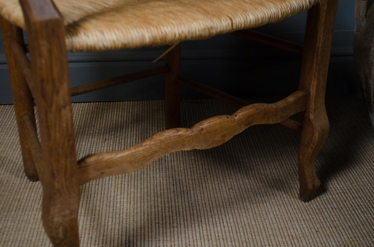 Close-up of a rustic wooden chair leg and woven seat on a textured beige rug.
