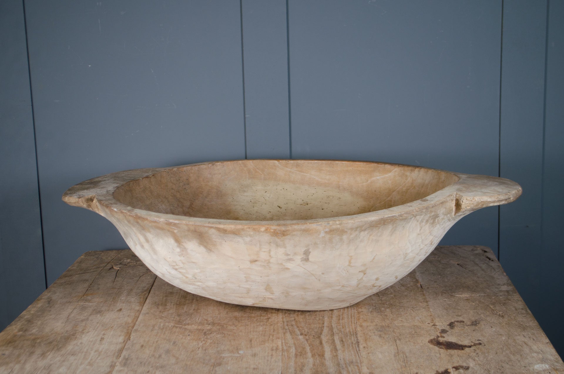 
Pair of antique wooden dough bowls with carved handles, pale waxed surface and rustic texture displayed on table