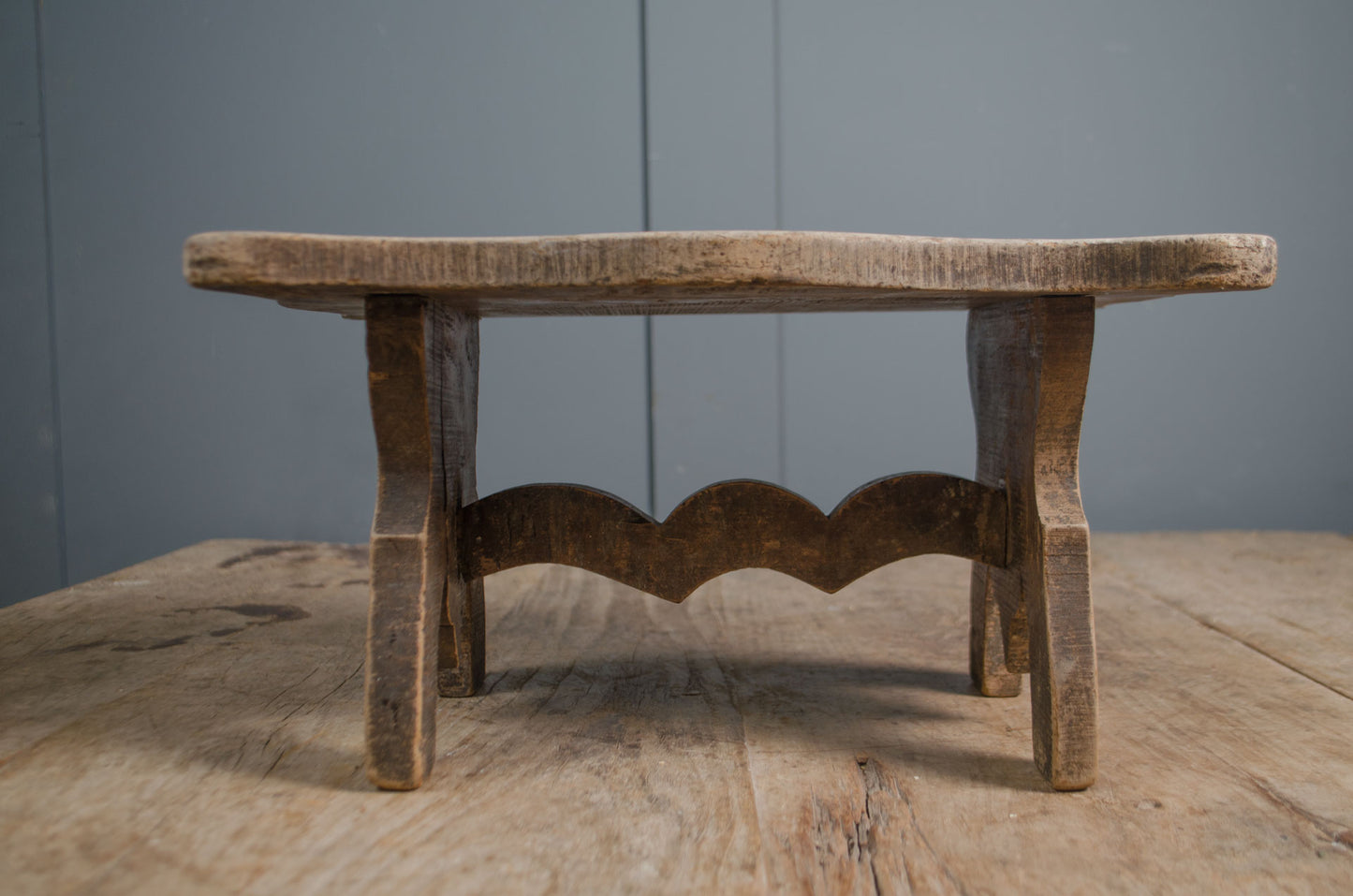 Primitive French wooden stool with weathered grey finish and carved rustic base on wooden table