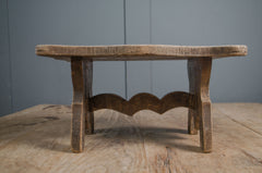 Primitive French wooden stool with weathered grey finish and carved rustic base on wooden table