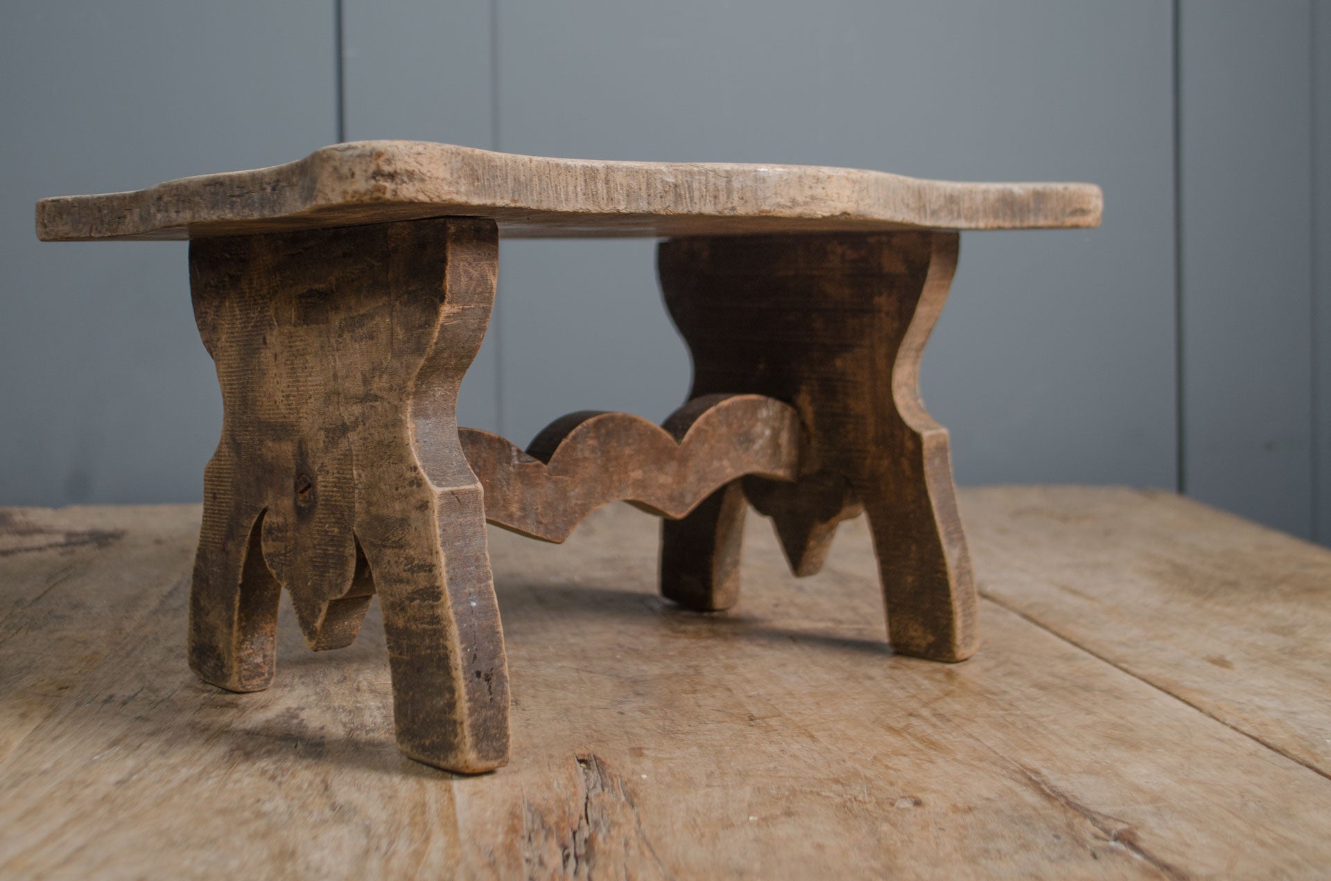 
Primitive French wooden stool with weathered grey finish and carved rustic base on wooden table