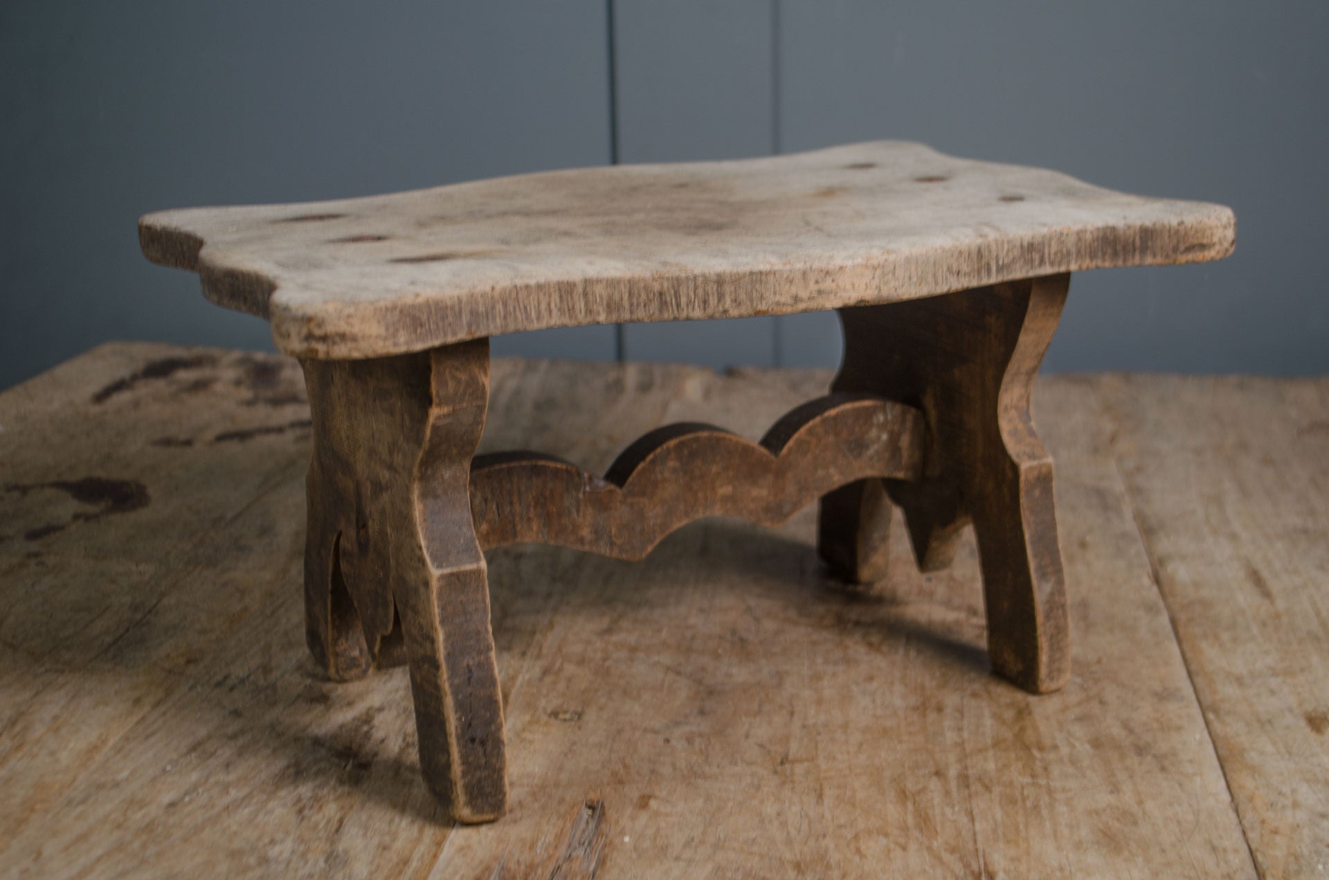
Primitive French wooden stool with weathered grey finish and carved rustic base on wooden table