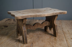 Primitive French wooden stool with weathered grey finish and carved rustic base on wooden table
