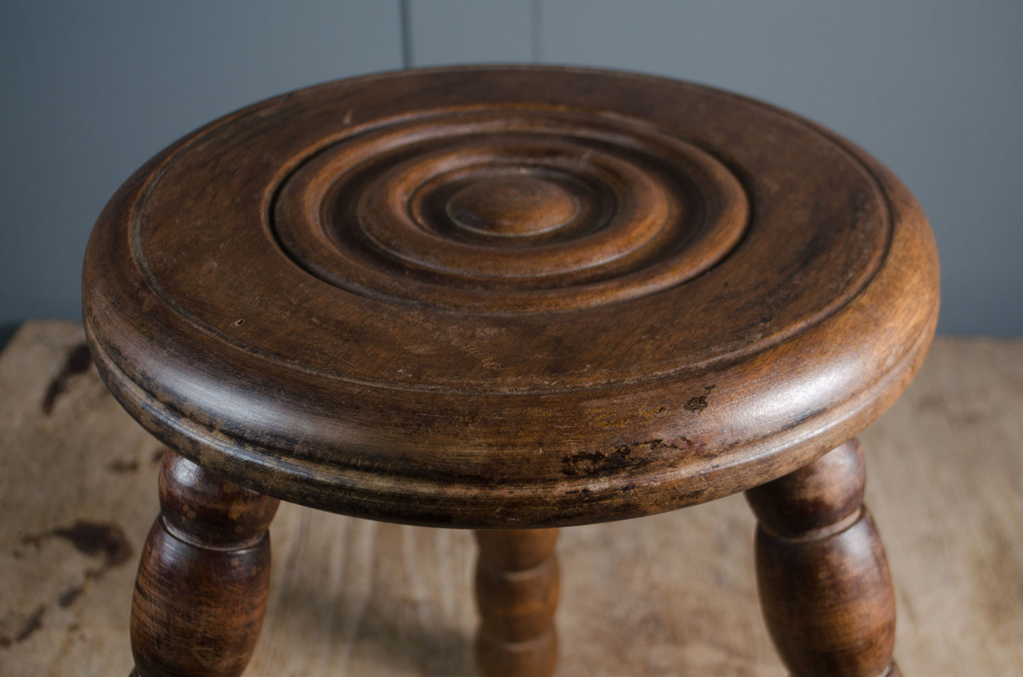 Wooden stool with a spiral design on a wooden surface against a gray wall.