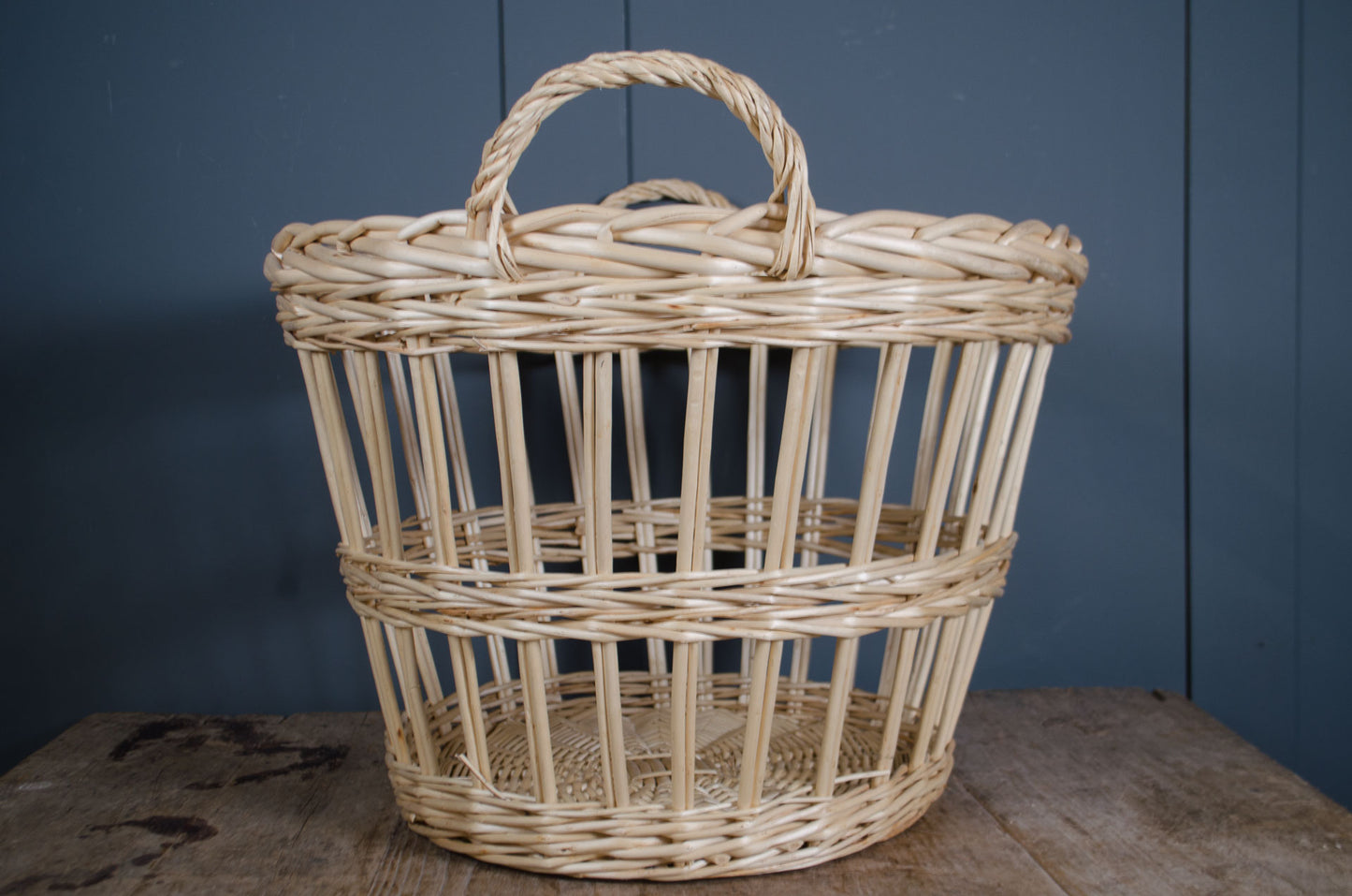 Wicker basket with handle on a wooden surface against a blue wall